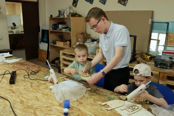 Наставник помогает детям в инженерной мастерской